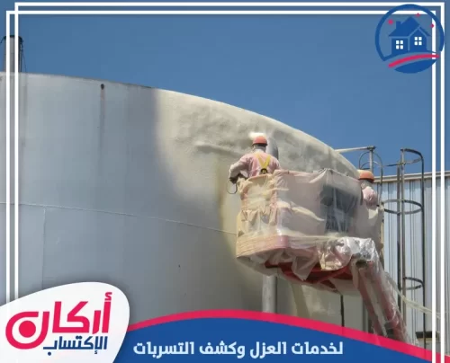 فني يرتدي بدلة واقية كاملة أثناء رش مادة عازلة سوداء (بيتومين) على جدران خزان خرساني من الداخل